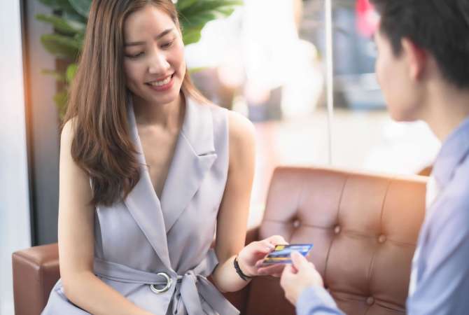 Salesperson workin at car dealership.Young Asian male consultant and couple buyers signing contract for new car in auto show. Concept for car rental or sale .Payment bt credit card.